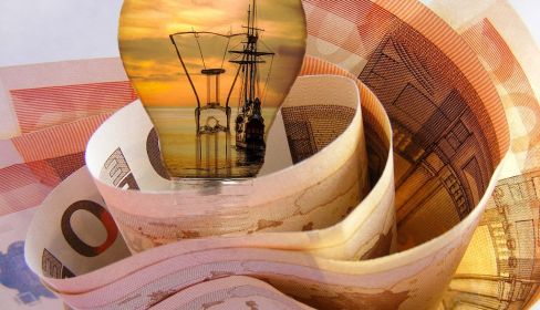 Una bombilla con un velero dentro y un fajo de billetes de 50€. Pixabay.