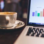Una taza de café, con la pantalla de ordenador y graficas. Imagen de StockSnap en Pixabay