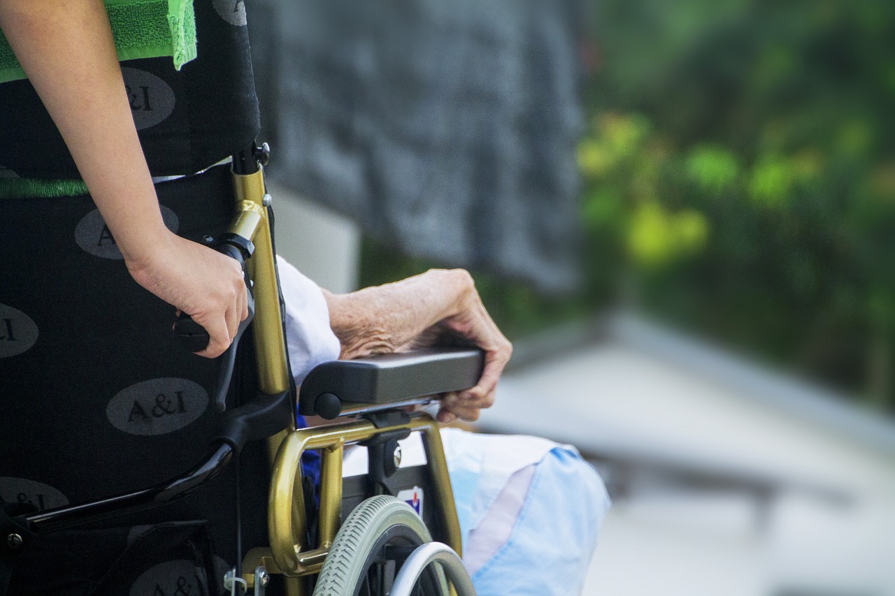 Una auxiliar de ayuda a domicilio llevando una silla de ruedas.