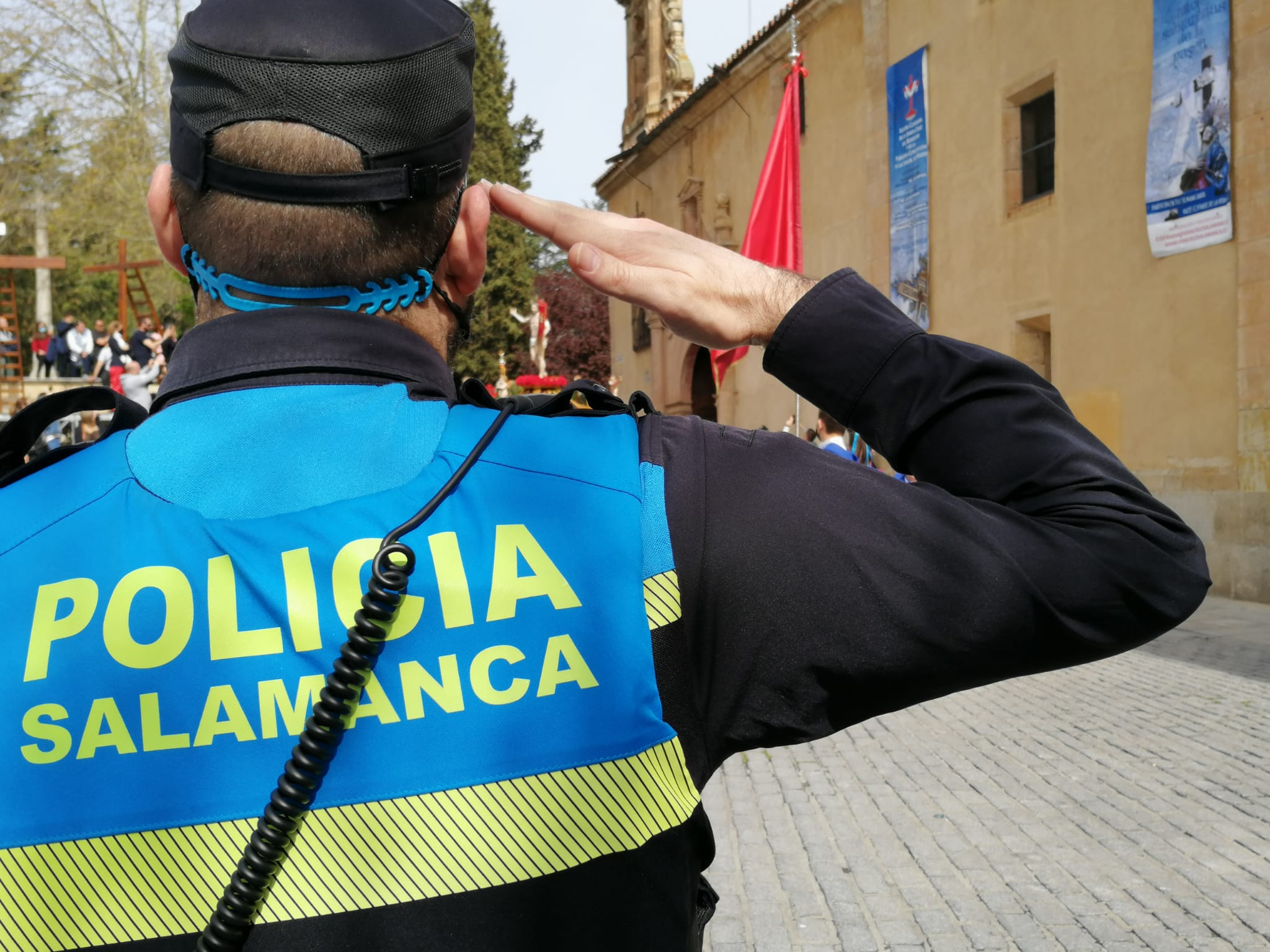 Un policía local saluda, al fondo el paso de Jesús Resucitado.